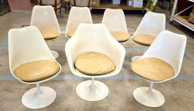 Six chaises « Tulip » blanches, dotées de coussins beiges, sont disposées dans une pièce