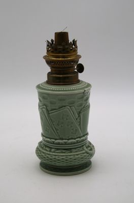 un petit vase vert avec un couvercle doré, posé sur une surface blanche