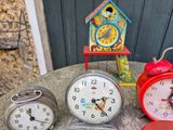 three clocks sitting on a table next to a birdhouse