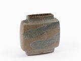 un petit vase posé sur une surface blanche