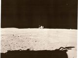 photographie en noir et blanc d'un astronaute sur la Lune, avec une navette spatiale en arrière-plan