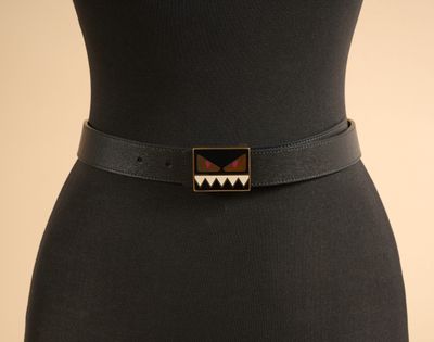 une femme vêtue d'une robe noire et d'une ceinture noire ornée d'un motif géométrique