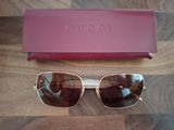 Lunettes de soleil Gucci et leur étui posés sur une surface en bois