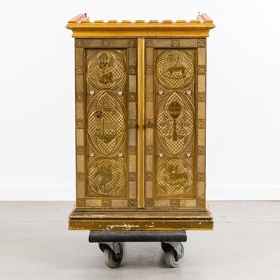 une armoire ancienne en bois montée sur roulettes, dans une pièce aux murs blancs