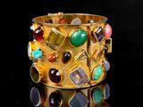 gold bracelet with multi colored stones and gems on a black surface