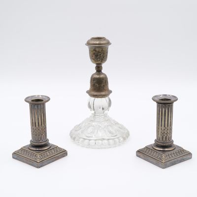 deux bougeoirs en argent et un bougeoir en verre sur fond blanc