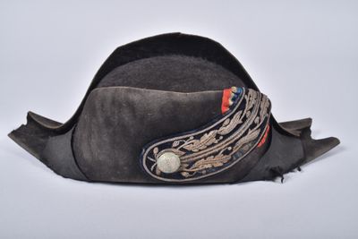 un chapeau gris orné d'une plume sur le côté, posé sur une surface blanche