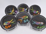 six assiettes noires sur lesquelles sont peints des oiseaux colorés, posées sur une table