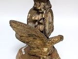 a statue of a bird on a base with a vase in the background