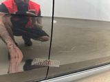 a man kneeling on the ground in front of a car looking at his cell phone