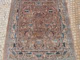 un tapis persan ancien posé sur un sol en briques, avec une personne debout à côté