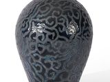 a black vase with a pattern on it on a white surface