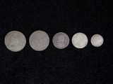 five silver coins in a row on a black surface