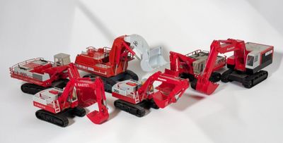 cinq camions rouges miniatures alignés sur une surface blanche