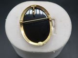 a close up of a black and gold broochle on a white stone