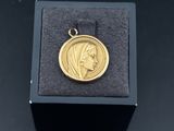 une petite médaille en or sur laquelle est représenté le visage d'une femme