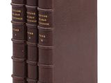 trois livres marron sont empilés les uns sur les autres sur une surface blanche
