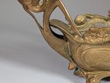 a gold vase with a bird on it on a white surface