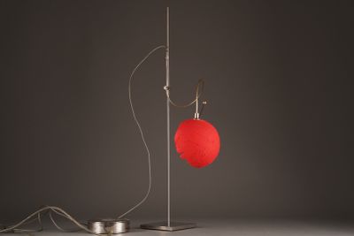 a red heart shaped lamp on a metal stand next to a wire