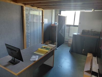 un ordinateur posé sur un bureau, dans une pièce où s'entassent de nombreux papiers