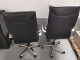 pair of black leather office chairs with chrome wheels and casteors