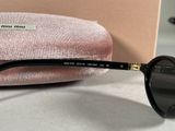 black sunglasses with gold trim and black lenses sitting on a pink velvet case
