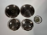 four silver dishes and a glass on a white surface
