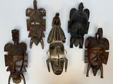 quatre masques en bois accrochés à un mur sur fond blanc