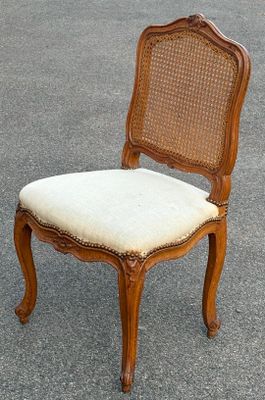 une vieille chaise avec un dossier et une assise en rotin, posée sur le trottoir