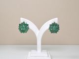 une paire de boucles d'oreilles vertes posées sur un présentoir blanc, sur une table blanche