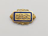 a close up of a gold and blue broochle on a white surface