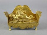 a gold figurine of a woman laying on a couch