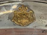 silver plate with a gold emblem and a crown on top of it