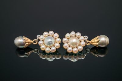 une paire de boucles d'oreilles en perles et en or posées sur un fond noir