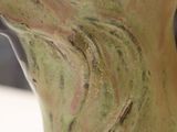 a green vase with a bird on it on a table