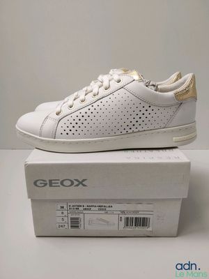une paire de baskets blanches et dorées posées sur une boîte blanche