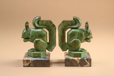 two green sculptures of animals on marble bases against a beige background