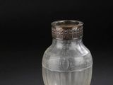 un vieux vase en verre muni d'un couvercle en argent, posé sur une surface noire