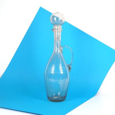 une bouteille en verre bleue avec une poignée argentée, posée sur un morceau de papier bleu