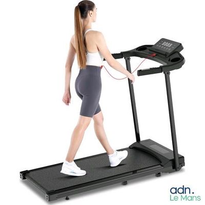 La femme marche sur un tapis roulant, un téléphone à la main.