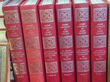 Plusieurs livres rouges sont empilés sur une table rouge, devant un fond rouge.