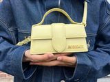 woman wearing a denim jacket holding a yellow handbag in front of a brick building