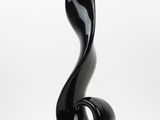 sculpture en verre noir posée sur un socle transparent, sur fond blanc