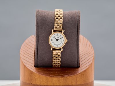 a gold watch sitting on a wooden stand on a table