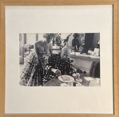 photographie en noir et blanc d'une femme assise à une table, avec une assiette de nourriture devant elle