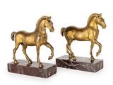 une paire de statues de chevaux en or sur des socles en marbre, sur fond blanc