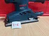 une ponceuse orbitale Bosch posée sur une table, à côté d'une boîte rouge