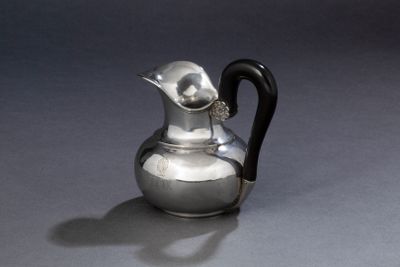 une cruche en argent avec une anse noire posée sur une table