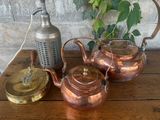 three copper kettles on a wooden table next to a teapot