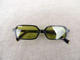 sunglasses on a white cloth with a black frame and a green lens